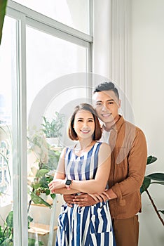 Happy young Asian couple looking through window at home