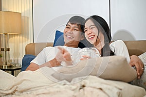 A happy young Asian couple in pajamas is enjoying watching television or a movie together in bed