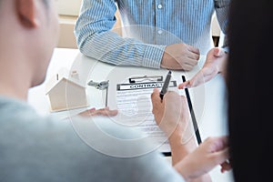 Happy young Asian couple and realtor agent. Cheerful young man signing some documents while sitting at desk together with his wife