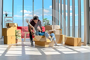 Happy young asian couple smiling relaxing and having fun while playing with cardboard box in new house celebrating moving to new