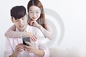 Happy young Asian couple using mobile phone , browsing internet, chatting online, relaxing on sofa at home