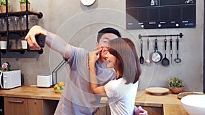 Happy young Asian couple using smartphone for selfie while cooking in the kitchen at home. Man and woman preparing healthy food.