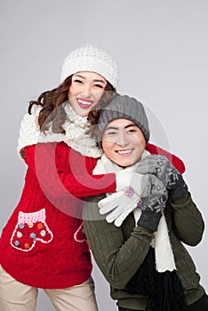 Happy young asian couple wearing knitted warm scarf, over gray b