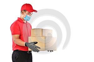 Happy young Asian delivery man in red uniform, medical face mask, protective gloves carry cardboard box in hands isolated on white