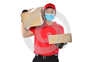 Happy young Asian delivery man in red uniform, medical face mask, protective gloves carry cardboard box in hands isolated on white