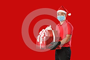 Happy young Asian delivery man in red uniform, medical face mask, protective gloves, Christmas hat carry boxes of presents in hand