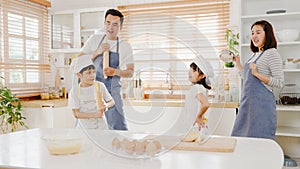 Happy young Asian family with preschool kids have fun listen to music and dancing while cooking baking pastry for breakfast meal