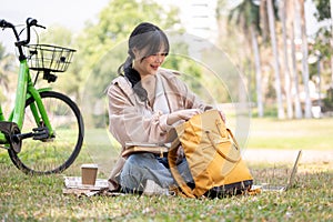 A happy young Asian female college student is chilling in a campus park, doing her homework