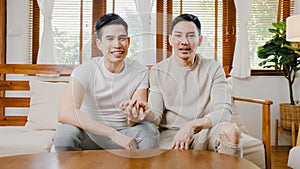 Happy young asian gay couple sit couch use smartphone facetime video call with friends and family in living room at home. Stay at