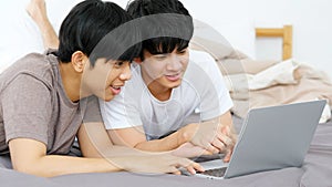 Happy young asian gay man couple using laptop computer while lying on bed at home, homosexual and lgbt with technology lifestyle