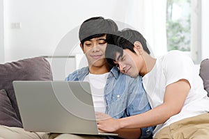 Happy young asian gay man couple using laptop computer while sitting onsofa at home, homosexual and lgbt with technology lifestyle