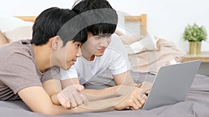 Happy young asian gay man couple using laptop computer while sitting onsofa at home, homosexual and lgbt with technology lifestyle