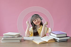 A happy young Asian girl enjoys listening to music on her headphones at her study table