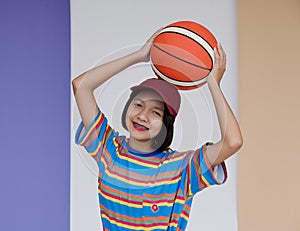 Happy young asian girl palying basketball with pastel background