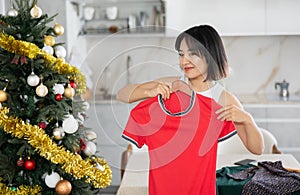 Happy young Asian girl trying to choose a dress standing next to Xmas-tree