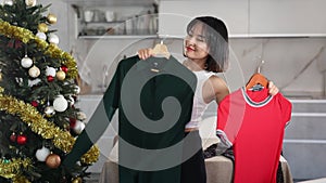 Happy young Asian girl trying to choose a dress standing next to Xmas tree in the kitchen