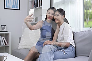 Happy young Asian lesbian couple taking selfie in the living room. LGBT couple lifestyle concept