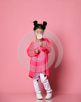 Happy young asian little girl kid lick eat happy big sweet lollypop candy on pink