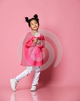 Happy young asian little girl kid lick eat happy big sweet lollypop candy on pink