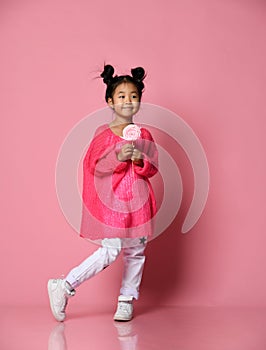 Happy young asian little girl kid lick eat happy big sweet lollypop candy on pink