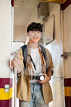 A happy young Asian male traveler backpacker is getting off the train, arrived at his destination