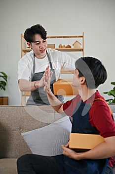 A happy young Asian man giving high fives to his boyfriend while working at home together
