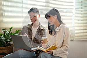 A happy young Asian man and a pretty girl are working on a laptop together, sharing ideas