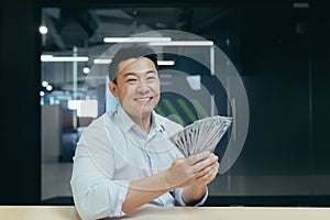 Happy young Asian man received salary in cash. He holds money in his hands, shows it, rejoices