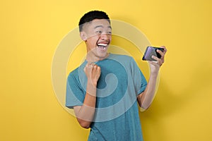 Happy Young Asian man smiling holding a smartphone and looking at phone screen, getting discount at online store application