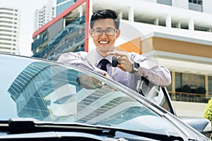 Šťastný mladý ázijský muž zobrazené z nový auto 