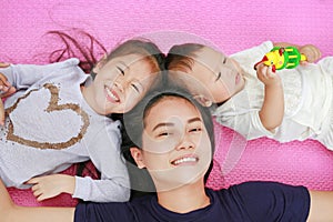 Happy Young Asian mother daughter and son lying on pink mattress mat looking at camera. View from above