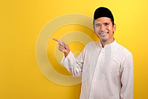 Happy Young Asian muslim man pointing to showing a copy space presenting something