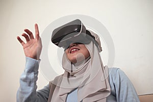 Happy young Asian muslim woman playing on VR glasses. Virtual reality concept with a girl having fun with headset goggles