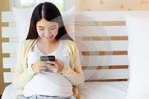 Happy young asian pregnant woman using and browsing online information of prenatal care on smartphone. Pregnancy mother sitting on