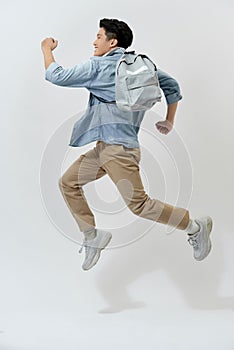 Happy young Asian student man jumping in the air with backpack over white background
