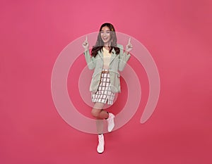 Happy young Asian teen woman standing with her pointing finger up isolated on pink background with copy space