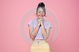 Happy young Asian teenage girl holding hands in pray near mouth on pink background