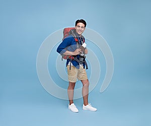 Happy young Asian tourist man holding passport with backpack going to travel on holidays isolated on blue background