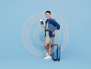 Happy young Asian tourist man holding passport with baggage going to travel on holidays isolated on blue background