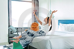 Happy young Asian traveler woman relax on bed in hotel room. Travel alone, summer and holiday concept