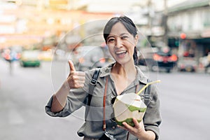 Happy young Asian woman backpack traveler drinking a coconut juice at China town street food market in Bangkok, Thailand. Traveler