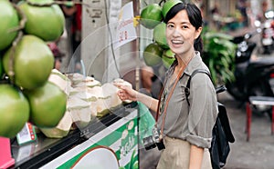Happy young Asian woman backpack traveler stand in front of coconut juice shop at China town street food market in Bangkok,