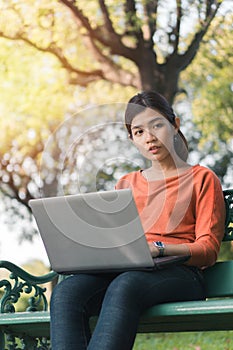 Happy young asian woman be smile working with her laptop on a bench in the park outdoors on vacation time