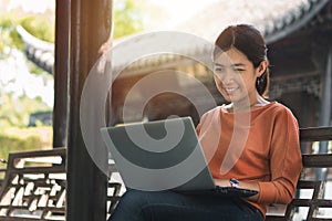 Happy young asian woman be smile working with her laptop on a bench in the park outdoors on vacation time