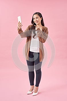 Happy young asian woman casually dressed standing isolated over pink background, using mobile phone