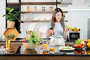 A happy young Asian woman choosing and preparing a healthy salad with vegetables on the home kitchen counter.