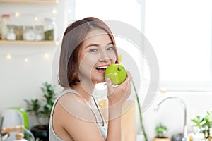 Happy Young Asian Woman Eating Green Apple on Kitchen. Diet. Die