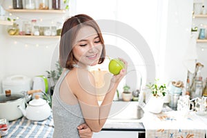 Happy Young Asian Woman Eating Green Apple on Kitchen. Diet. Die