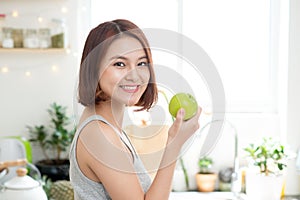 Happy Young Asian Woman Eating Green Apple on Kitchen. Diet. Die