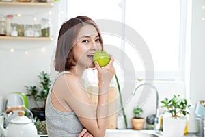 Happy Young Asian Woman Eating Green Apple on Kitchen. Diet. Die